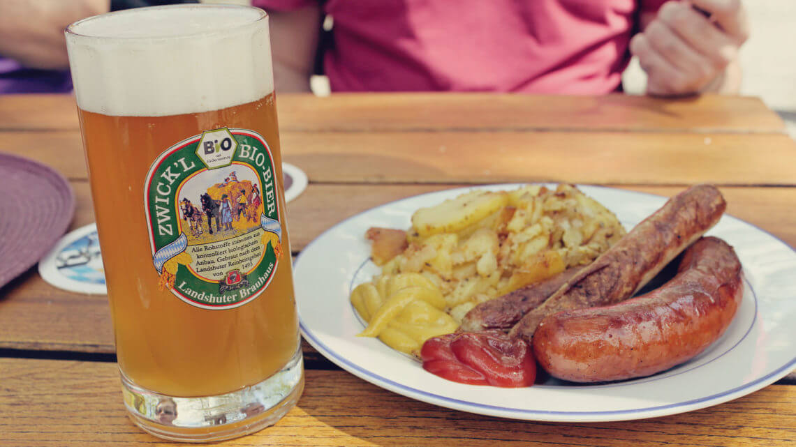 Cervejas e viagens 5 destinos para beber - bar em Munique com cerveja em uma caneca e prato tradicional de salsicha com batatas