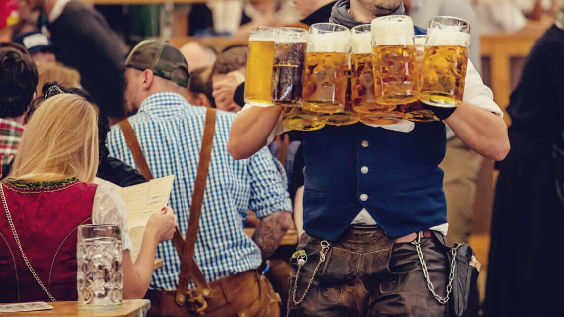 Tour de Cerveja em Munique: Homem carregando diversos copos grandes de cerveja em roupas tradicionais da Bavária