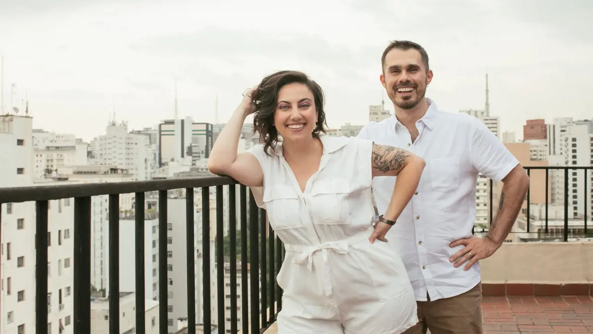 Natalie e Fred lado a lado vestidos de branco no terraço com a vista de São Paulo ao fundo
