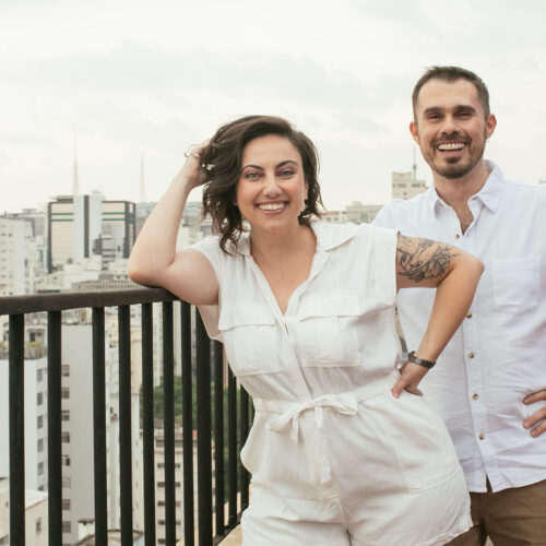 Natalie e Fred lado a lado vestidos de branco no terraço com a vista de São Paulo ao fundo