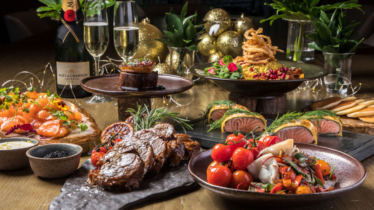 Brunch de Natal em uma mesa de madeira com carnes assadas, ceviche, sashimi de salmão e duas taças de champagne