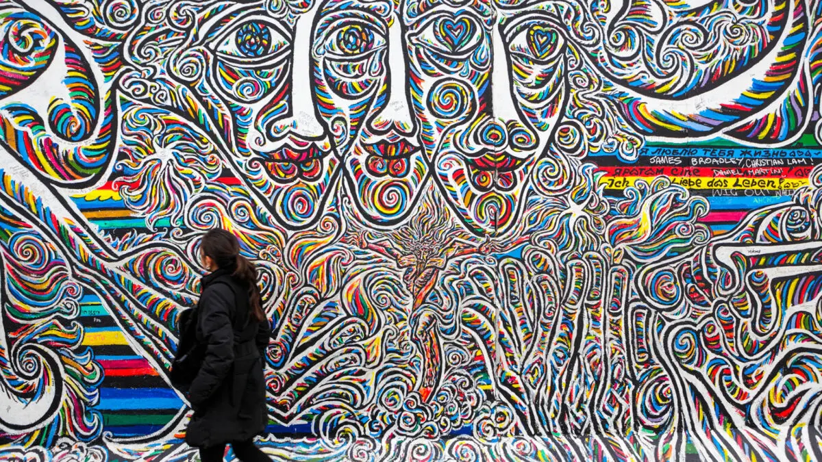 Uma mulher aprecisando as cores vibrandes da East Side Gallery, uma das maiores galerias a céu aberto de arte de rua em Berlim