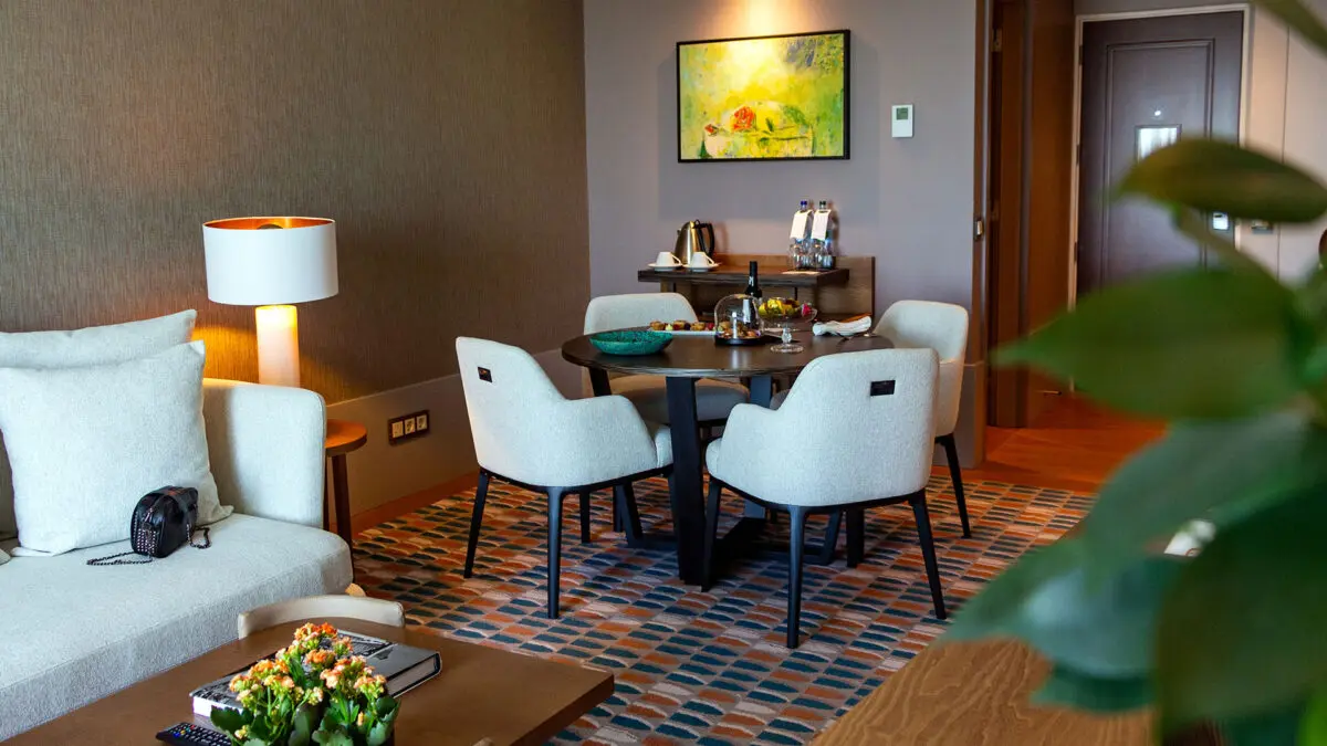 Sala com sofá cinza e mesa com quatro cadeiras confortáveis são um dos pedacinhos do quarto no Corinthia Lisbon 