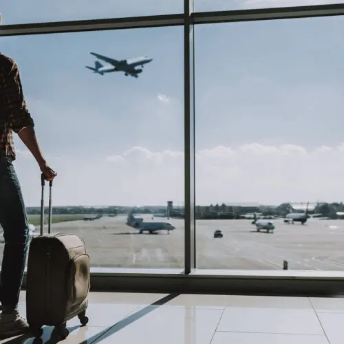 Viajante olhando o avião decolando pelo vidro da sala de espera do aeroporto