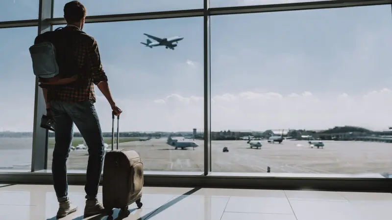 Viajante olhando o avião decolando pelo vidro da sala de espera do aeroporto