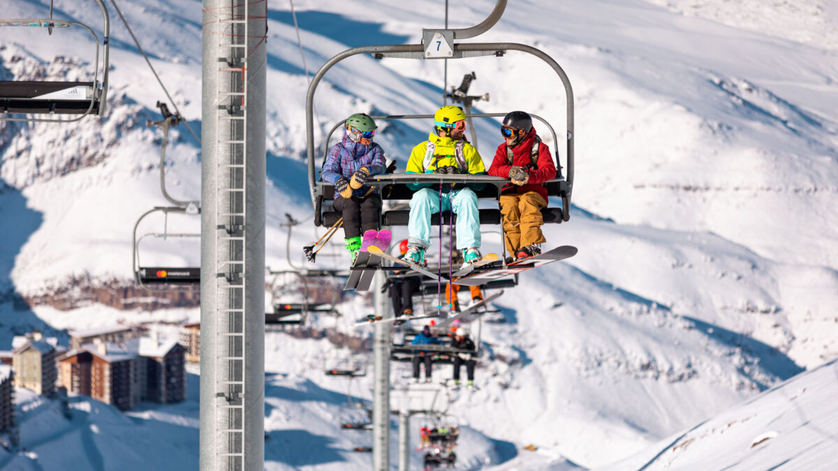 Três visitantes usando o teleférico com equipamentos de esqui