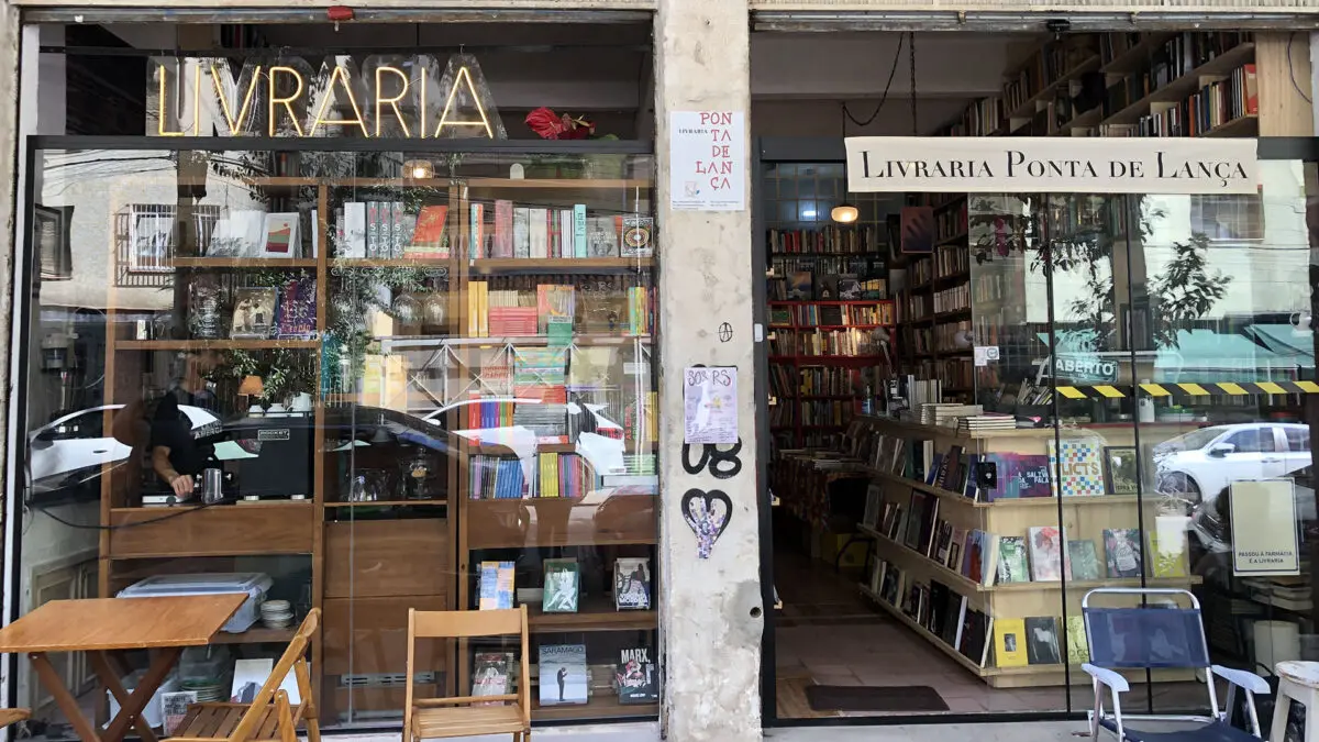 Fachada da pequena livraria Ponta de Lança, com cadeiras e mesas na calçada em frente à vitrine de livros